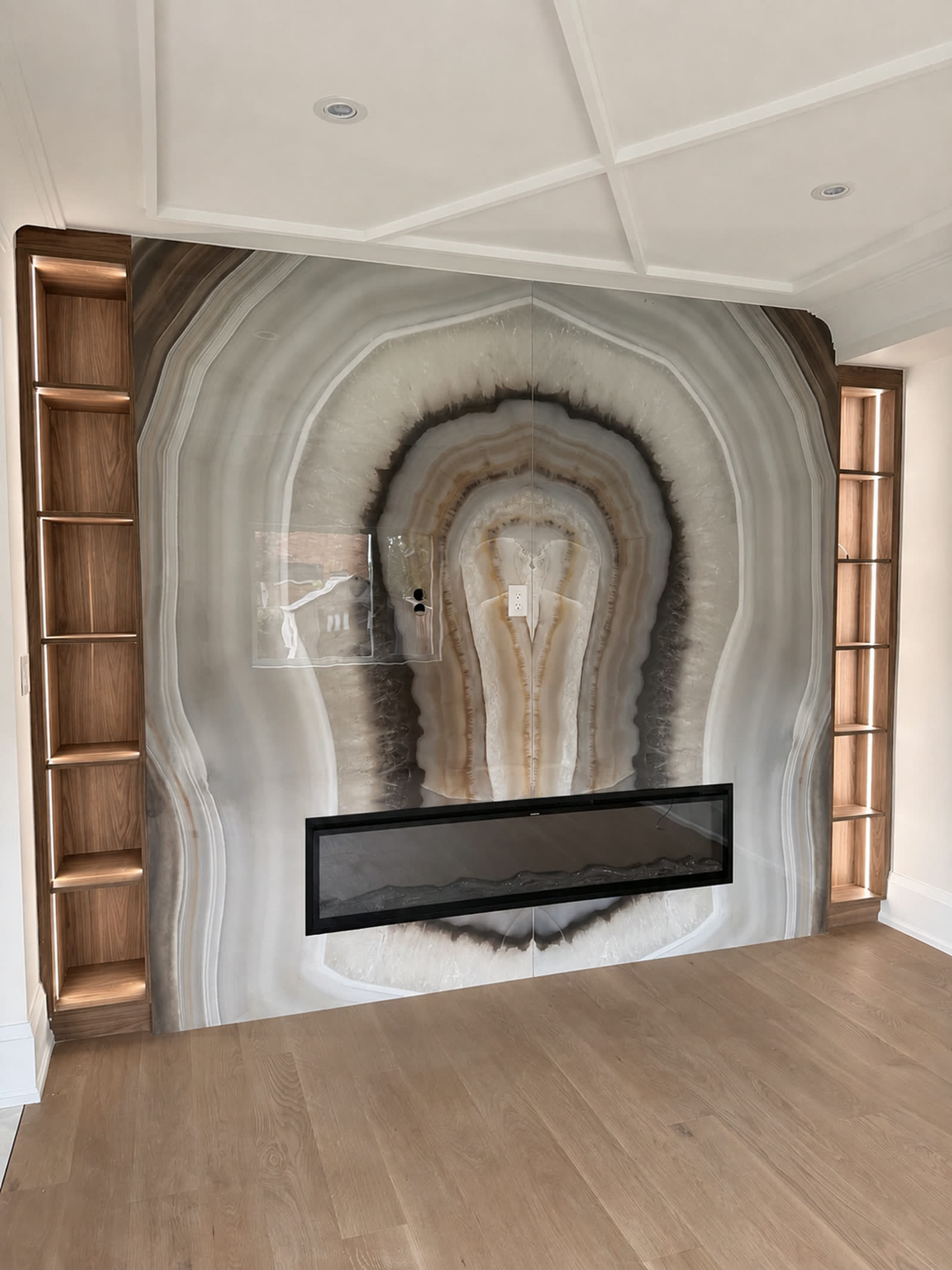Book matched onyx feature wall with a linear fireplace and lit walnut display niches